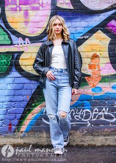 a woman standing in front of a wall with graffiti on it and wearing ripped jeans