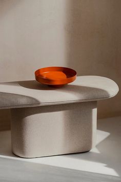 an orange bowl sitting on top of a white table next to a wall and floor