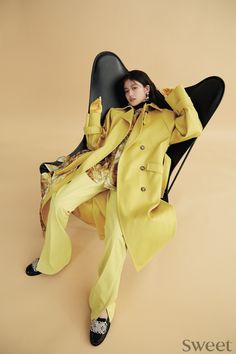 a woman sitting on top of a chair wearing a yellow coat and matching pants with black shoes