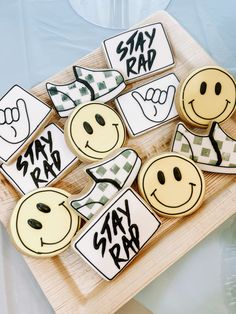 cookies decorated with smiley faces and words on a wooden platter for someone's graduation party