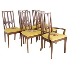 six wooden chairs with yellow upholstered seats and floral embroidered seat covers on them