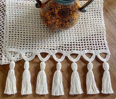 a crocheted table runner with tassels and a tea pot on it