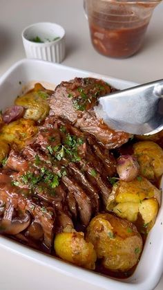 a white dish filled with meat and potatoes