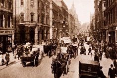 an old black and white photo of people walking down the street with horse drawn carriages