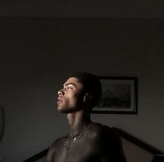 a man standing in the dark with his eyes closed and no shirt on, looking up