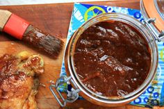 a jar of barbecue sauce next to a piece of bread on a wooden cutting board