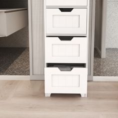 three white drawers sitting on top of a hard wood floor next to a cabinet door