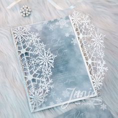 two cards with snowflakes on them sitting on a fur covered surface next to some beads