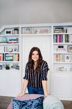 a woman sitting on top of a bed next to a blue and white pillow in front of a bookshelf