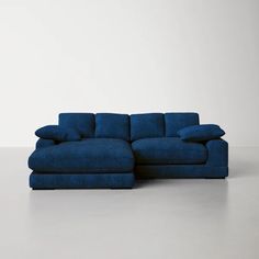 a blue sectional sofa with pillows on the top and bottom, in front of a white wall