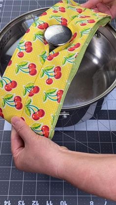 a person holding a spoon in front of a pot holder with cherries on it