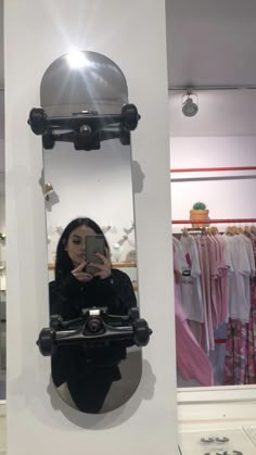 a woman taking a selfie in front of a mirror with clothes hanging on the wall