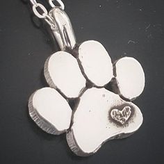 a silver dog paw with a heart in the center on a black surface, it appears to have been made into a pendant