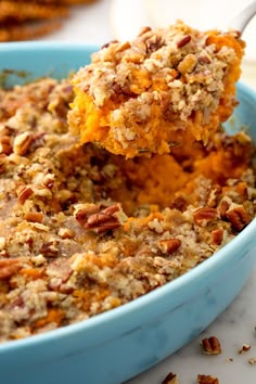 a blue bowl filled with sweet potato casserole topped with pecans and crumbs