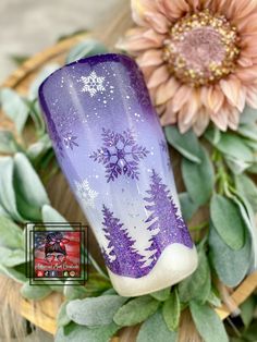 a purple vase sitting on top of a wooden table next to flowers and greenery