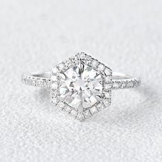 an engagement ring with a diamond center surrounded by pave diamonds on a white background