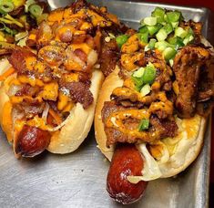 two hot dogs covered in toppings sitting on top of a metal tray next to each other