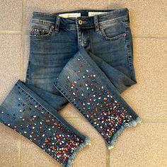 two pairs of jeans with multicolored sequins on them sitting on the floor