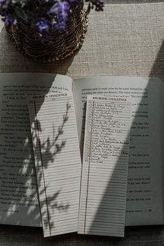 an open book sitting on top of a table next to a basket filled with flowers