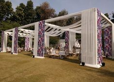 an outdoor wedding set up with white draping and purple flowers on the side