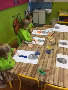 three children sitting at a table with paper and paint