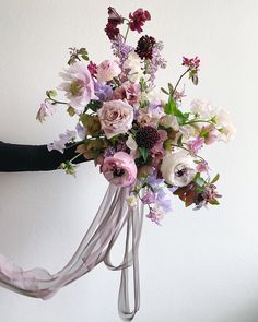 a woman holding a bouquet of flowers in front of a white wall with pink ribbons hanging from it