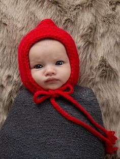 a baby wearing a red knitted hat on top of a blanket