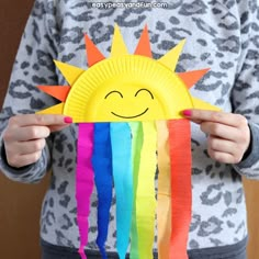 a child holding up a paper plate with a smiling sun on it