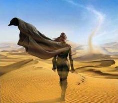 a man walking across a desert covered in sand with a long cape over his head