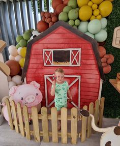 a little boy standing in front of a fake barn and farm animals at a birthday party