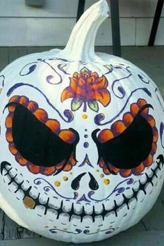 a white pumpkin decorated with black eyes and orange flowers sitting on the ground next to a chair