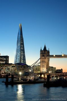 the tower bridge is lit up at night in front of the cityscape and skyscrapers