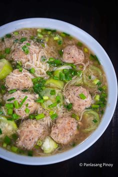 a bowl of soup with meatballs, green onions and broccoli in it