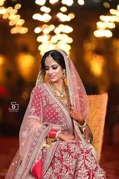 a woman sitting in a chair wearing a red and white bridal gown with gold jewelry