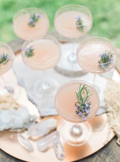 several glasses filled with pink liquid and lavender sprits on top of a table