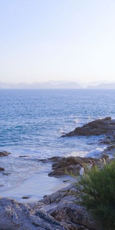 two people are sitting on the rocks near the water and looking out at the ocean