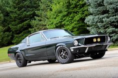 an old muscle car is parked on the side of the road in front of some trees