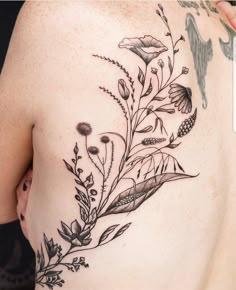 a woman's back with flowers and birds tattoo on her left side ribcage