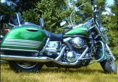 a green motorcycle parked on top of a grass covered field with trees in the background