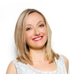 a woman with blonde hair smiling at the camera and wearing a white top, standing in front of a white background