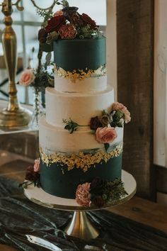 a three tiered wedding cake with flowers on the side and greenery on top