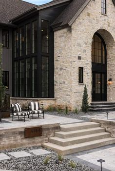 a stone house with black and white striped chairs on the front porch, steps leading up to it