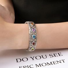 a woman wearing a bracelet with colorful stones on it