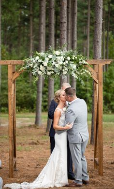 a bride and groom kissing in front of an outdoor ceremony arch with flowers on it