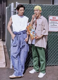 two young men standing next to each other near a fence with a no parking sign on it