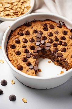 a chocolate chip cookie in a white bowl with one slice taken out and the other half eaten