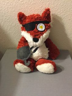 a red and white stuffed animal with sunglasses on it's face sitting on a table