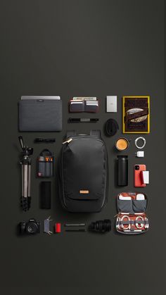 the contents of a black backpack laid out on a gray surface, including camera and other items