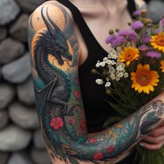 a woman with tattoos holding flowers and a dragon tattoo on her arm in front of some rocks