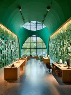 an office with green walls and desks in front of large glass windows that look out onto the outdoors